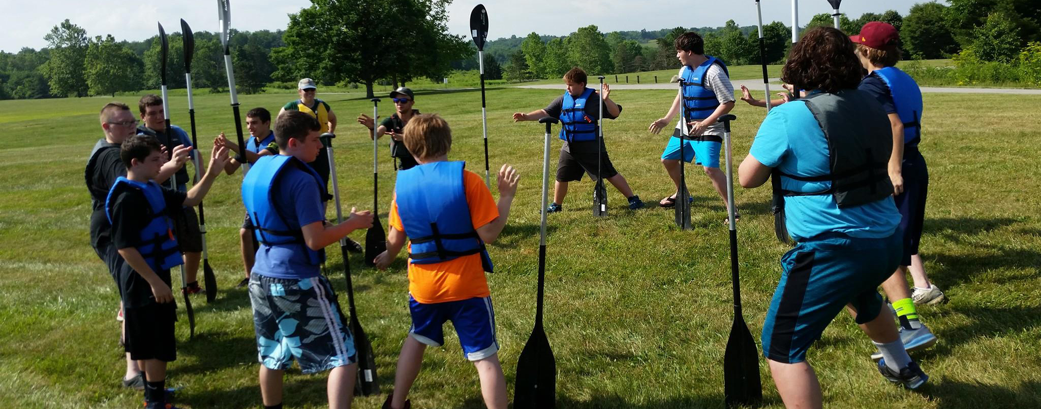 Kids standing in a circle holding canoe paddles and wearing life vests